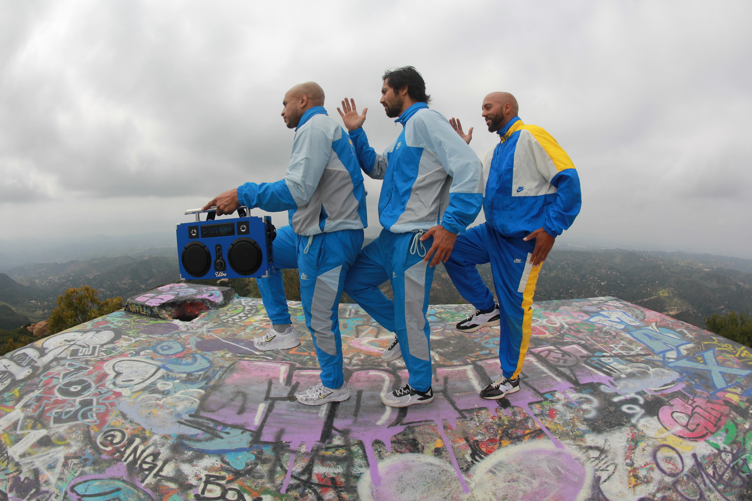 THEULTRABOYS dancing together with a blue boombox on a graffiti-covered hilltop